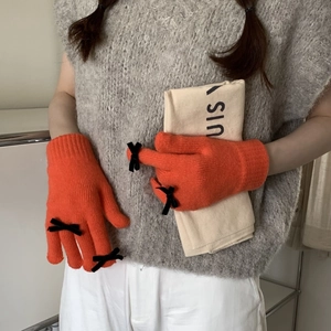Close-up of bright orange knitted gloves featuring black velvet bow and ribbed cuffs
