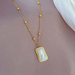 Gold titanium steel necklace with iridescent rectangular shell pendant on silk background