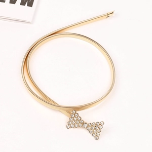 Détail d'une chaîne de taille en métal doré avec une boucle en forme de nœud en strass