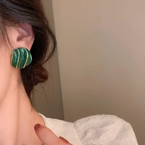 Close-up of vintage emerald green shell-shaped earrings with gold rim on model ear