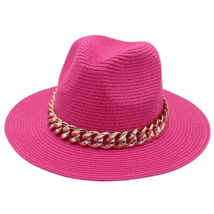 Détail du chapeau Panama fuchsia avec une grosse chaîne dorée sur texture tressée