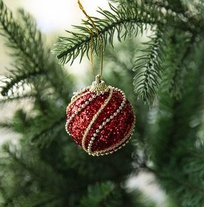 Macro detail of red sequined Christmas ball with gold bead spiral on green pine tree