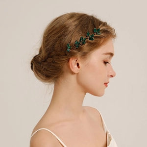Detail of a gold leaf hair pin with green crystals styled on a bridal hairstyle
