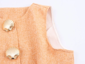 Détail de gilet en tweed orange avec texture tissée et boutons dorés en forme de coquille