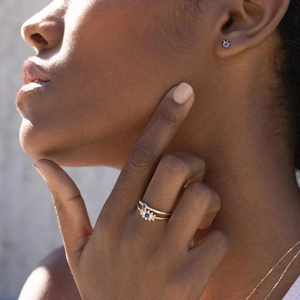 Close-up of gold stud earrings and rings set with blue gemstones worn by a model