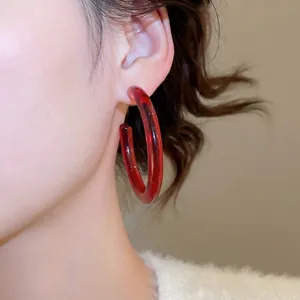Fashionable red translucent resin C-shaped hoop earrings worn by a model in a side view