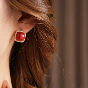 Close-up of square red gemstone earrings with gold plating and sparkling zircon accents