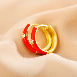 Macro detail of red enamel gold hoop earrings with sparkling rhinestones on satin