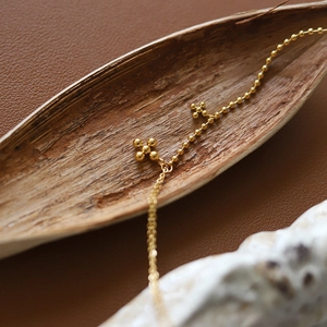Minimalist 18K gold plated beaded cross necklace on a dried leaf and leather background