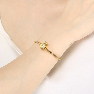 Close-up of golden snake chain bracelet with sparkling zircon crown charm on model wrist