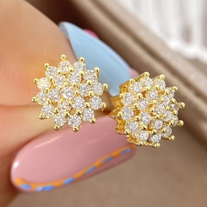 Golden sunflower stud earrings with cubic zirconia stones shown on finger for scale