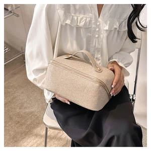 Detail of beige woven straw makeup bag with zipper closure and handle held by a model