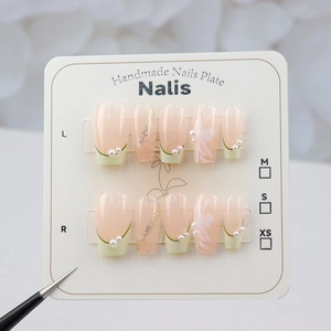 Detail of handmade press-on nails with white floral art, pearls and gold glitter lines