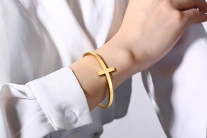 Detail view of a gold-plated stainless steel open cuff bracelet with a cross on the wrist