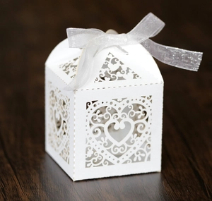 Detail of white laser-cut wedding candy box with heart pattern and organza ribbon