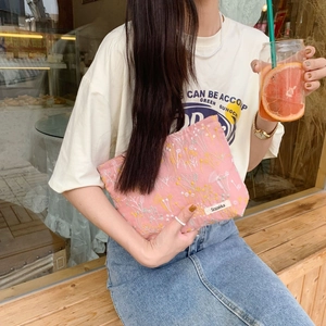 Outdoor lifestyle view of pink floral embroidery cosmetic bag held by a model
