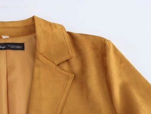 Détail du revers et de l'épaule du blazer en suédine moutarde avec étiquette de taille