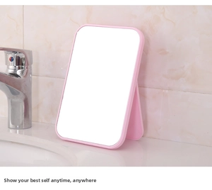 Pink portable folding makeup mirror with adjustable stand on a tiled bathroom counter