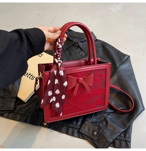 Detail of red bridal handbag with embroidery, 3D bow, and silk scarf on the handle