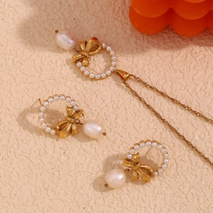 Detail of 18K gold bow necklace and pearl earrings set on a textured beige background