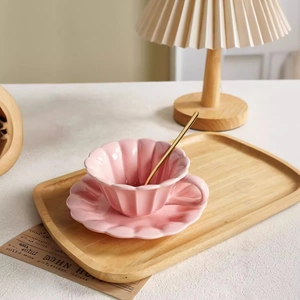 Pink ceramic coffee cup set with shell texture, gold spoon, and saucer on wood tray