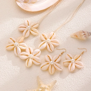 Dettaglio del set di gioielli con conchiglie e perle su sfondo di sabbia bianca