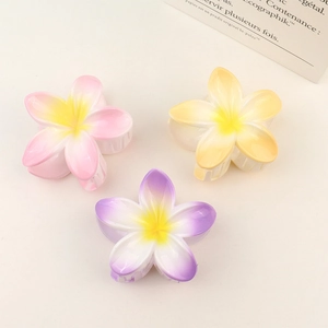 Three gradient resin plumeria hair claw clips in pink, orange, and purple on beige surface