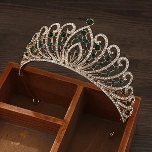 Baroque gold crown with green gems and rhinestones displayed on a rustic wooden box