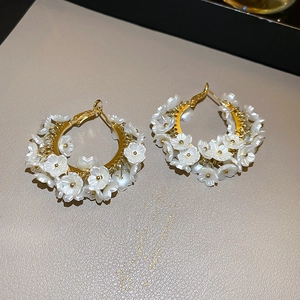 Detail of gold C-shaped hoop earrings with white flowers and pearls on textured surface