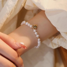 Close-up of white freshwater pearl bracelet with a golden heart pendant on wrist