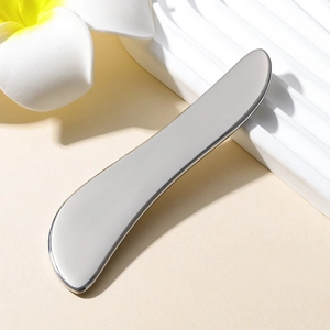 Polished heart-shaped stainless steel Gua Sha tool on a decorative base for facial massage