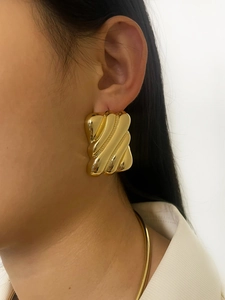 Detail of a textured golden square earring with geometric wavy surface worn by a model