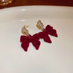 Macro detail of red velvet bow earrings with shimmering zircon and gold plating
