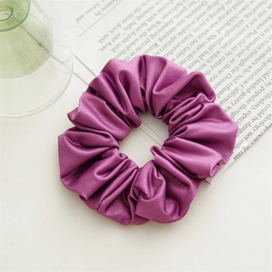 Detail shot of purple satin scrunchie with glossy texture and rich pleats on white desk