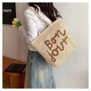 Detail of beige woven tote bag featuring brown bon jour embroidery and long shoulder strap