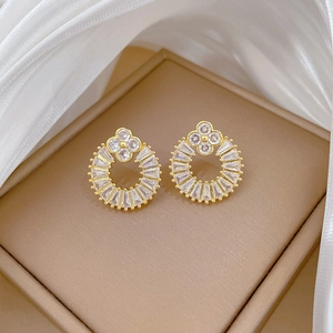Macro view of gold flower clover earrings with cubic zirconia on leather tray