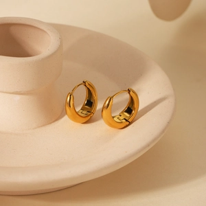 Detailed close-up of golden U-shaped chunky hoop earrings on a ceramic tray