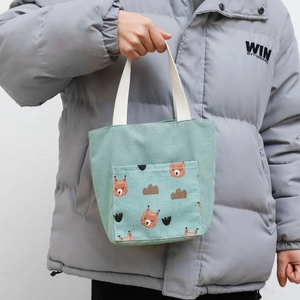 Detail of mint green canvas tote bag featuring a cute cartoon bear pocket and webbed handles
