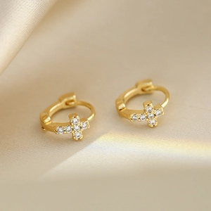 Macro shot of gold cross huggie earrings with clear cubic zirconia on silk fabric
