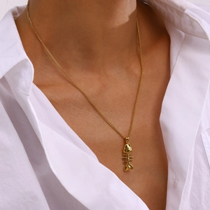 Gros plan d'un collier pendentif arête de poisson doré porté par un mannequin élégant