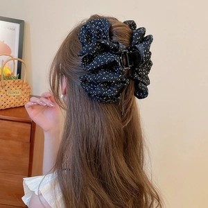 Détail d'une grande pince à cheveux noire en tissu à volants avec pois blancs