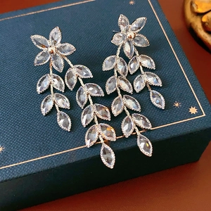Macro detail of silver flower and leaf earrings with clear crystals on blue box