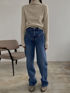 Detail of high-waist patchwork denim jeans paired with a beige turtleneck knit top
