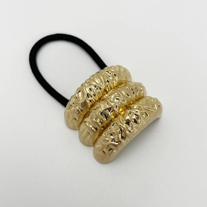 Detail of a black elastic hair tie with a gold three-layer wavy corrugated metal buckle