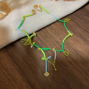 Detail of beaded flower necklace with green seed beads and gold lobster clasp closure