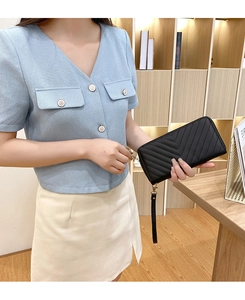 Detail of a black quilted leather long wallet with gold zipper and wristlet held by hand