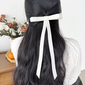 Close-up of a white ribbon bow hair clip worn on long wavy hair in a princess hairstyle