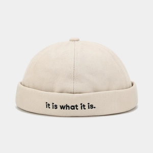 Detail of beige brimless cap featuring black letter embroidery and twill cotton fabric