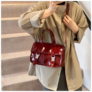 Detail of burgundy glossy leather tote bag with silver metal buckles on a model