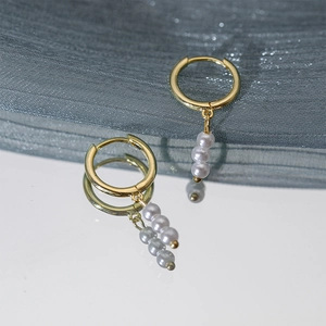 Detailed view of elegant gold hoop earrings with three hanging white pearls on mirror reflection